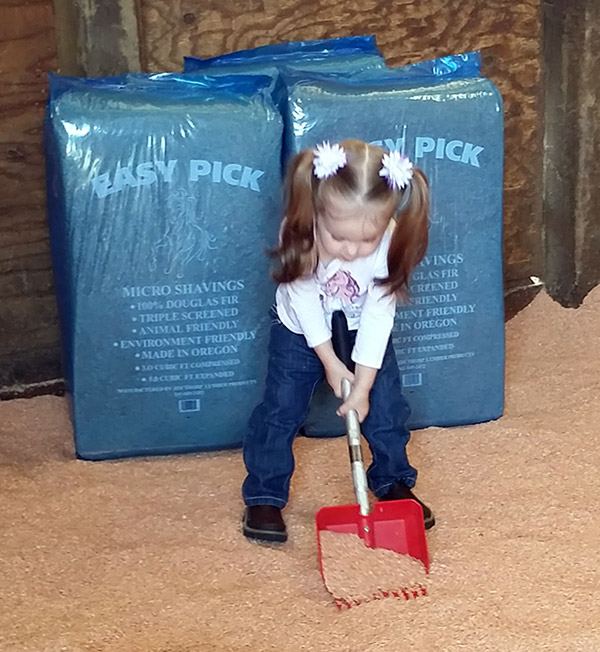 A young girl with a rake in front of stacked Easy Pick Shavings bags
